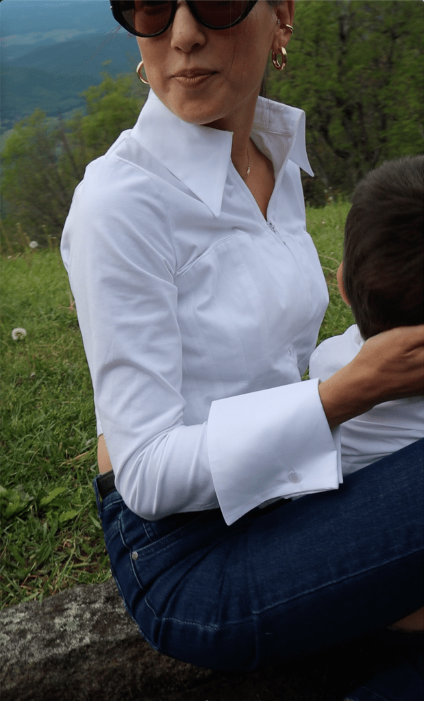 A woman wearing a stylish white shirt and denim jeans, seated on grass, enjoying a moment with a child.