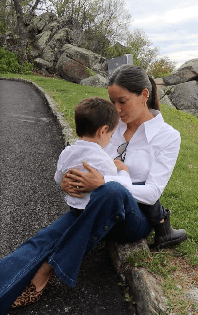 A mother in a white shirt embraces her young child in a natural outdoor setting, symbolizing the bond of motherhood.