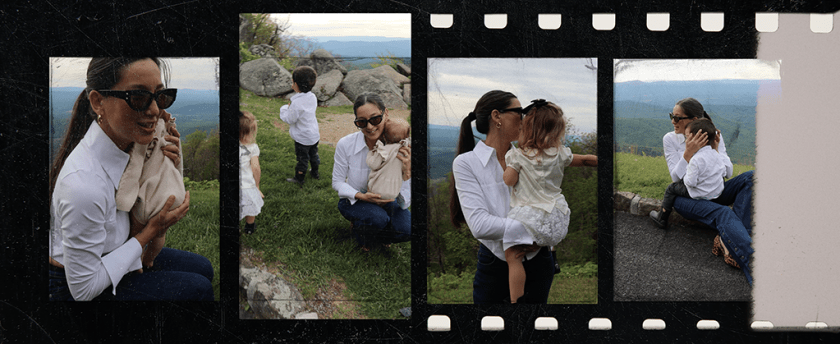 A woman in a white shirt is holding a baby while sitting on grass, with mountains in the background. Another child is seen in the distance, and a second woman is nearby.
