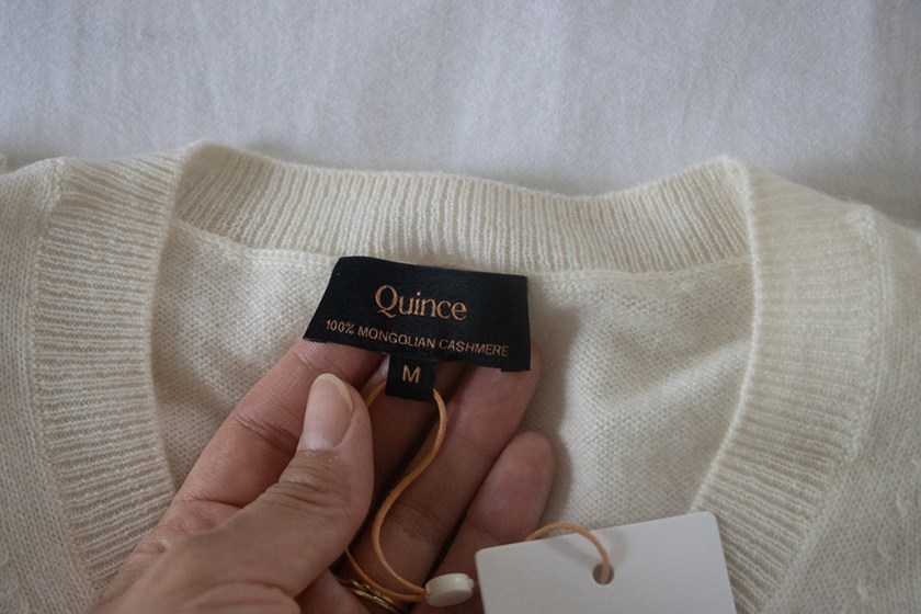 Close-up of a cashmere sweater label showing 'Quince', '100% Mongolian Cashmere', and size 'M'.