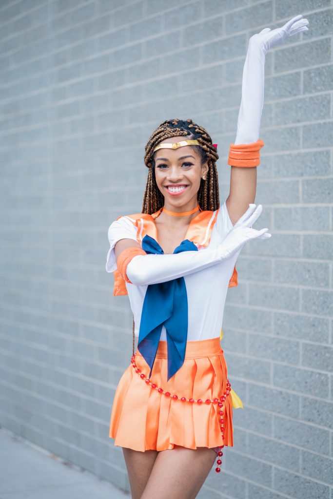 Black Woman dressed up as Sailor Venus - Orange Sailor Senshi Outfit and Love Chain | Halloween and Cosplay Ideas for women with Blonde Box Braids.