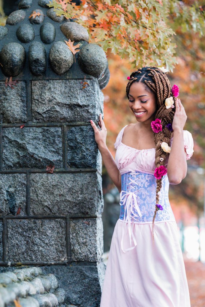 Black Woman Dressed as Disney's Rapunzel for Halloween - Blonde Box Braids with Fake Flowers in hair, Pink Dres, Purple Corset